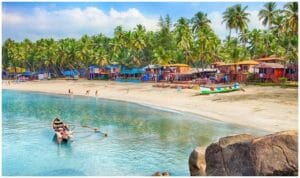 Panoramic view of palolem beach showing a few huts and many trees on te banks