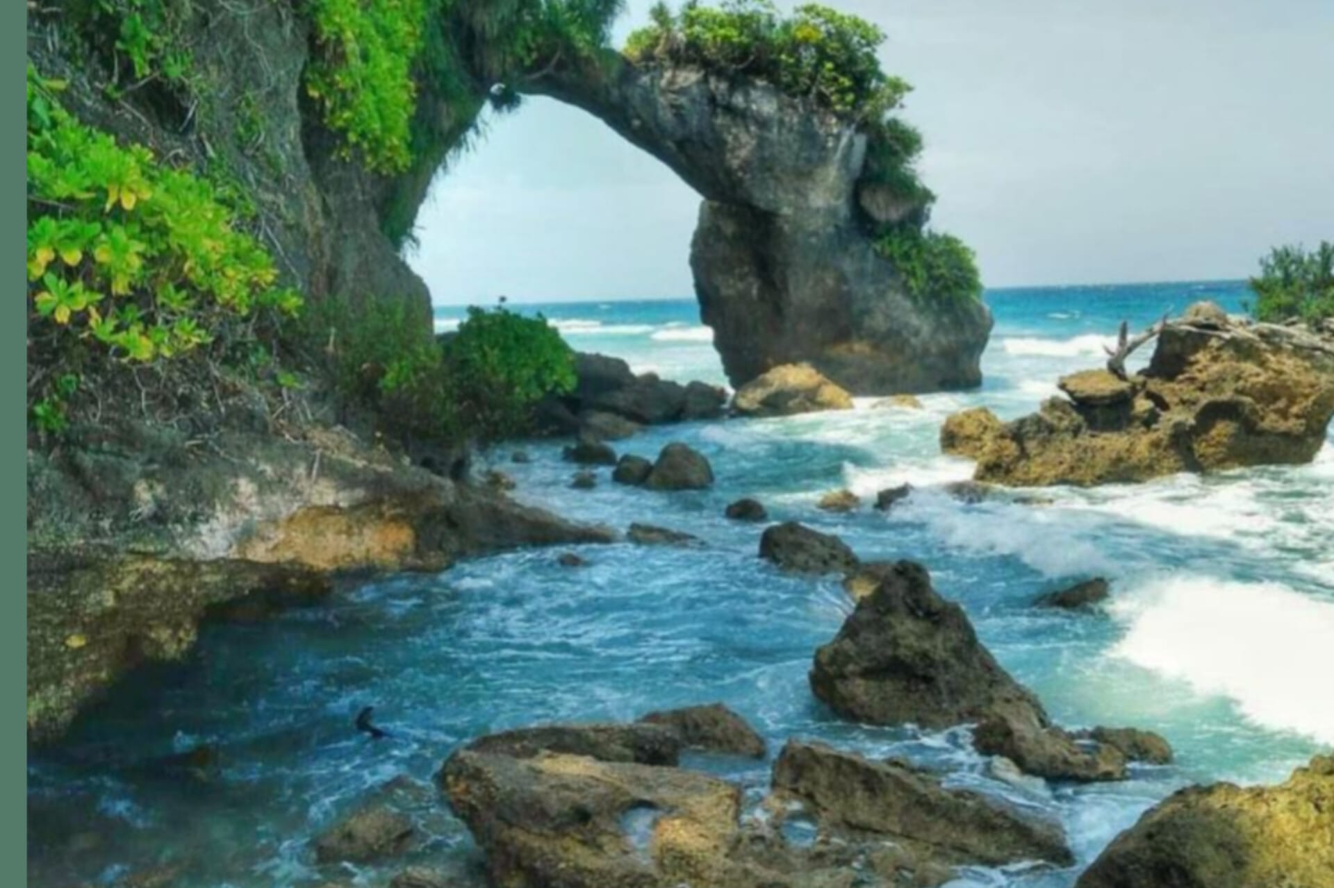 A grass covered rock cave and some stone in water