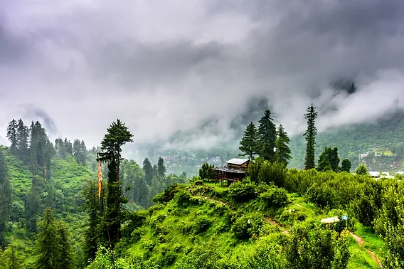 A green color mountain and has a small house on top of the mountain hill stations