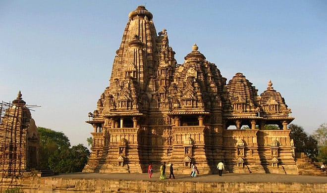 एक हल्का रंग का मंदिर जो बहुत ऊंचा है और इसपर सुंदर नक्काशी की गई है और कुछ लोग वहाँ पर खड़े हैं Madhya Pradesh Tourism