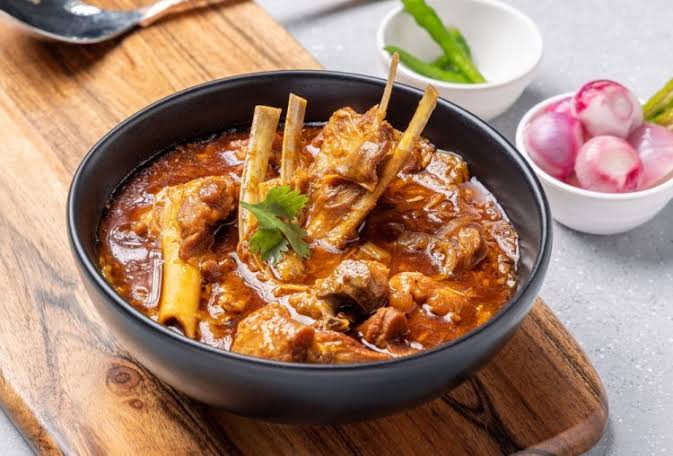 Mutton curry is kept on black bowl and onion is also present there in झारखंड के पारंपरिक व्यंजन:जो आपकी भूख को शांत कर देगी