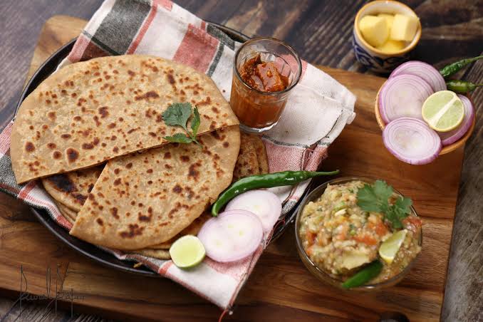 Sattu Paratha and green chilli one glass and some pieces of onion are there in बिहार के लोकप्रिय व्यंजन