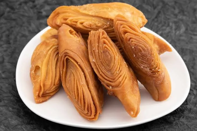 There are some pieces of yellowish color Khaja is kept in white plate बिहार के लोकप्रिय व्यंजन